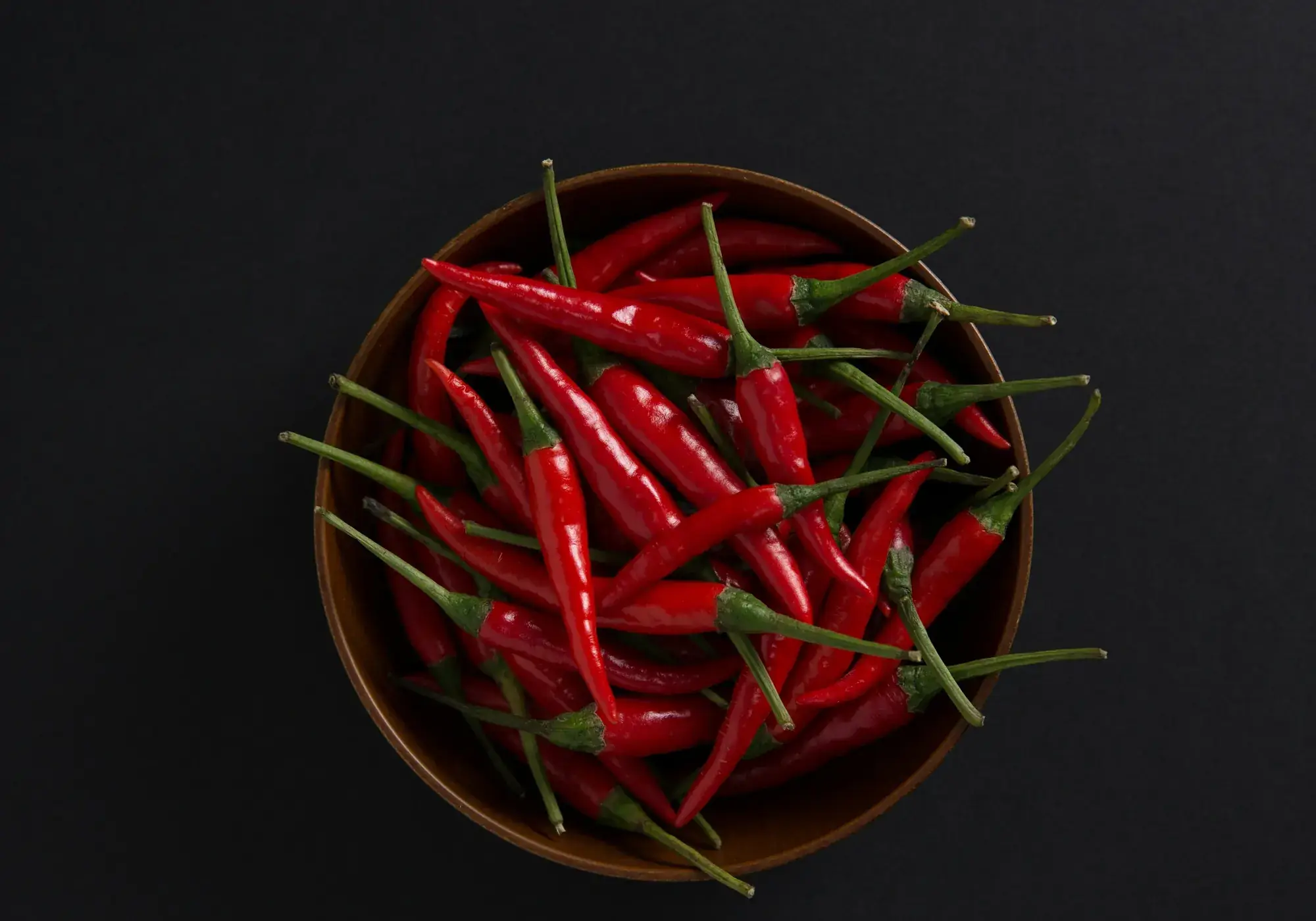 A dark bowl of long red chillies photographed from above on a near-black surface