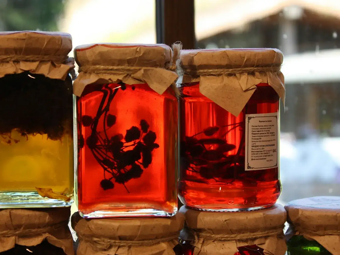 Jars of red preserve with paper-tied lids on a sunlit shelf
