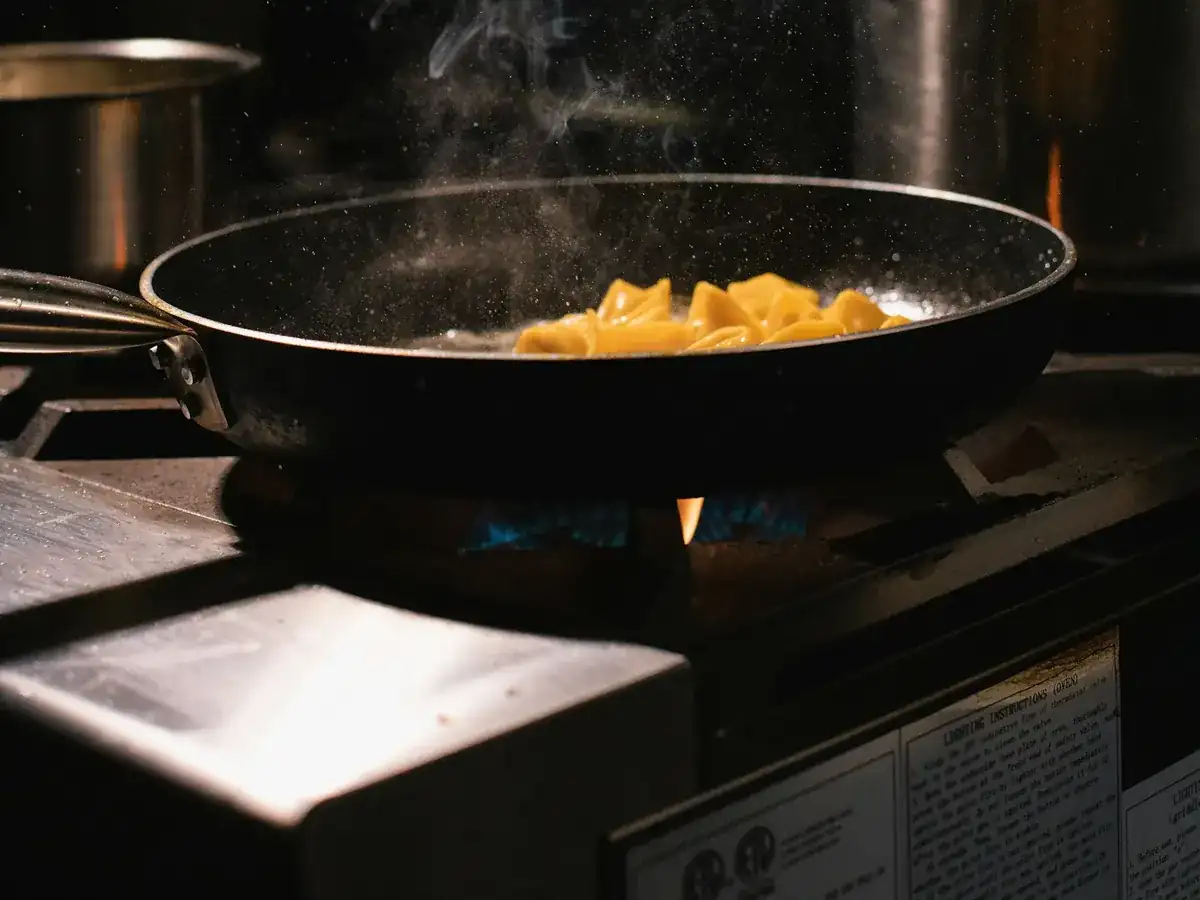 A chef reaching across a busy stove in a restaurant kitchen