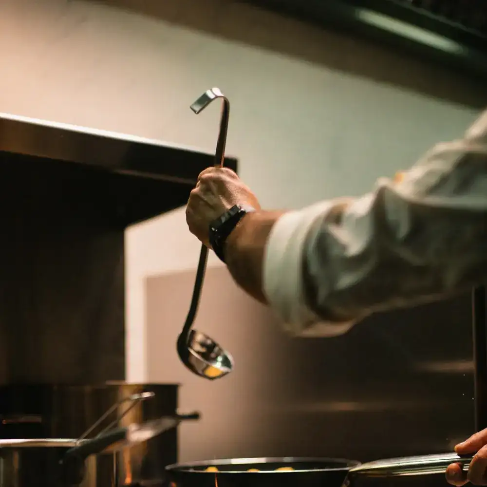 A cook finishing a plate by hand in a dark kitchen